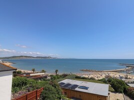 Vista costera con playa, un rompeolas rocoso y cielo azul despejado.