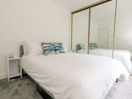 Un dormitorio con un espejo grande, una cama con ropa de cama blanca y una mesita de noche con un vaso de agua.