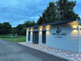 Un pequeño edificio azul claro con un logo de cisne y el nombre 'SWAN LAKE Lodge' en la fachada. Tiene dos puertas y un pequeño porche.