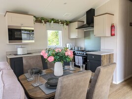 Una cocina compacta con microondas, estufa y lavamanos. Hay una mesa de comedor con sillas y un jarrón de flores.