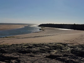 A coastal landscape with a sandy beach, rocky foreground, and a calm sea.