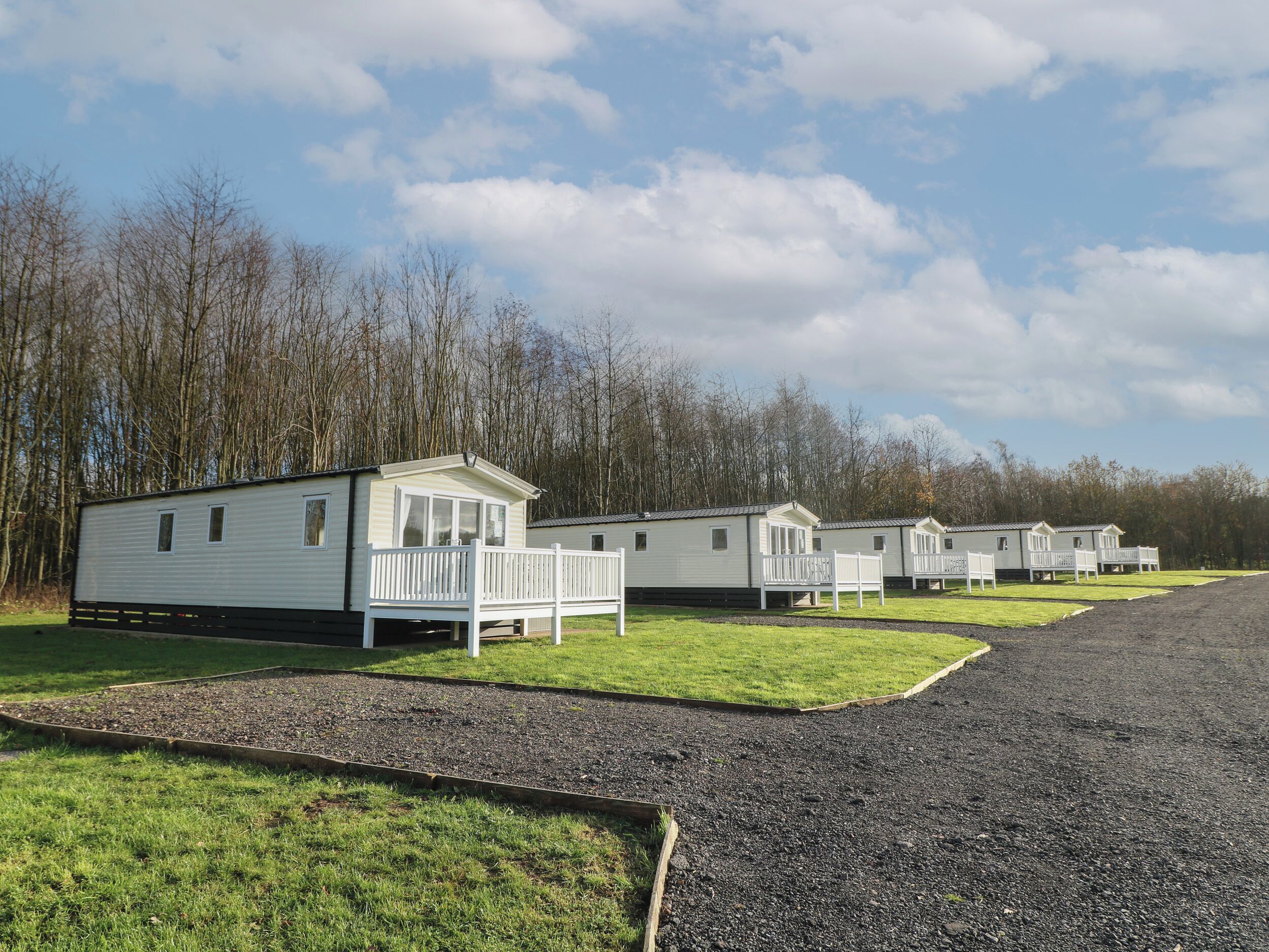 A row of mobile homes with attached porches, set against a backdrop of trees and a clear sky.