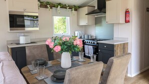 A compact kitchen with a microwave, stove, and sink. There is a dining table with chairs and a vase of flowers.