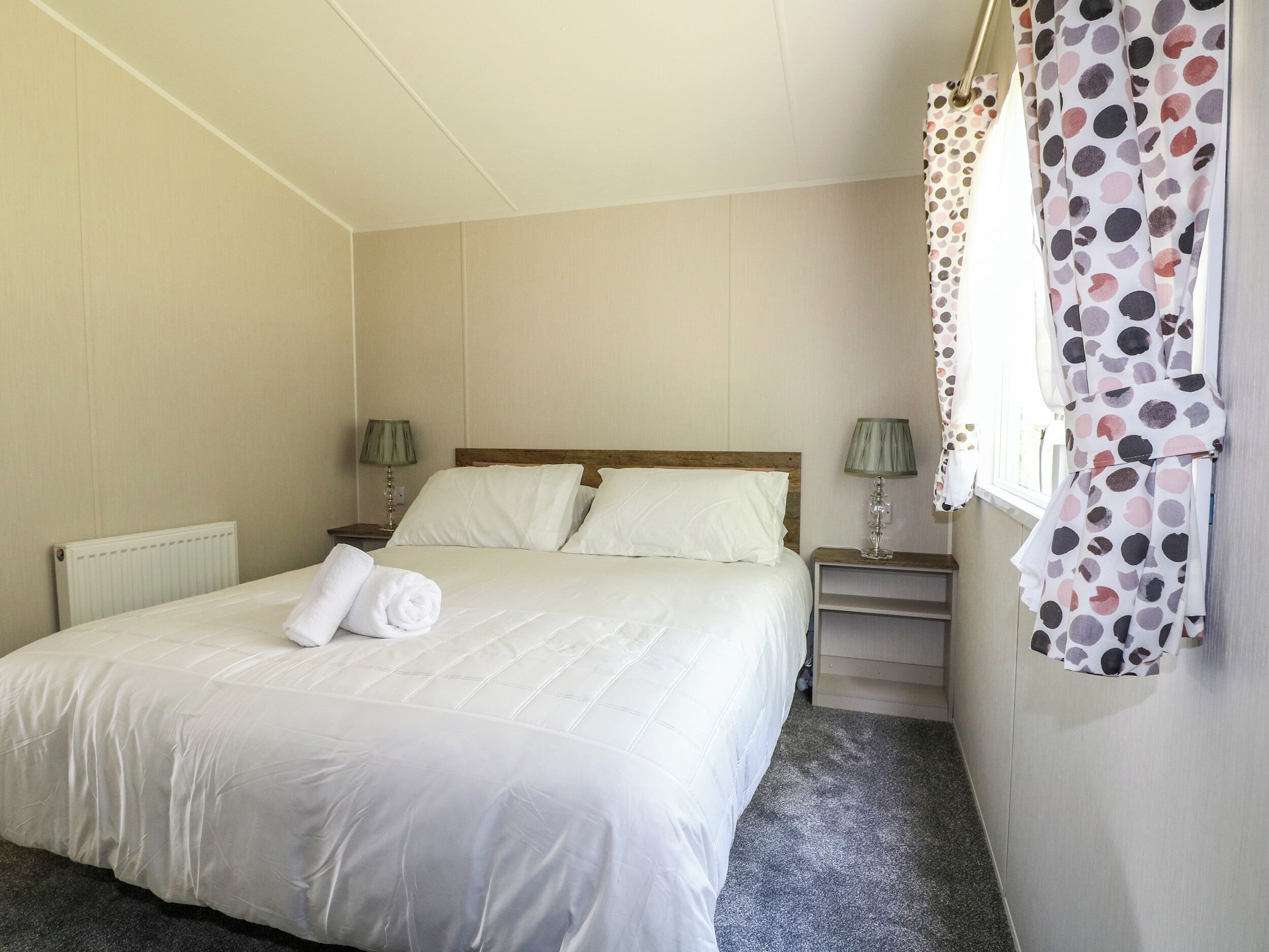 A neatly made bed with white linens, two bedside tables with lamps, and a polka dot curtain.
