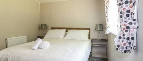 A neatly made bed with white linens, two bedside tables with lamps, and a polka dot curtain.
