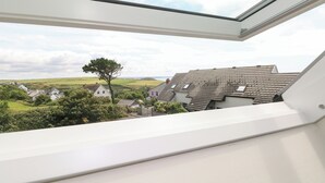 Vista desde una ventana a una zona residencial con casas, un árbol destacado y cielo despejado.