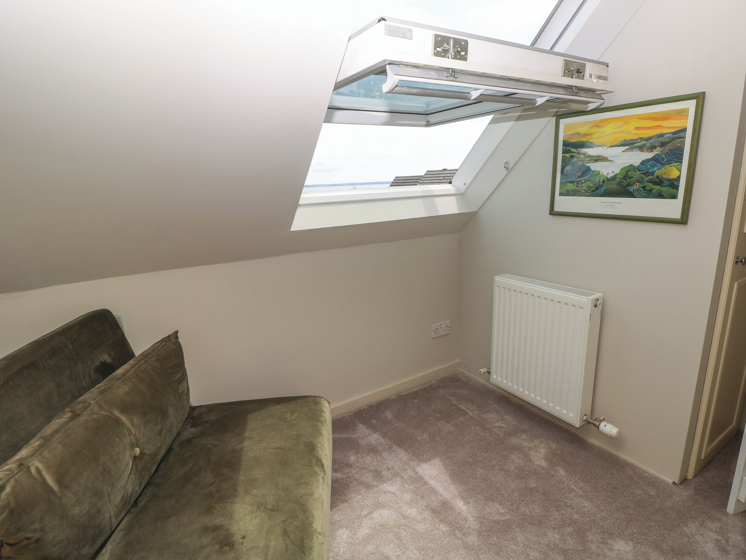 A room with a skylight, a radiator, a framed painting, and a green sofa.