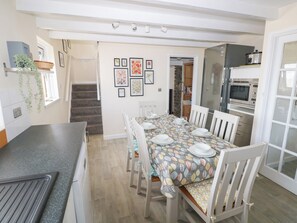 Comedor con una mesa preparada para cuatro personas, rodeada de sillas blancas, en una cocina con estufa y horno modernos.