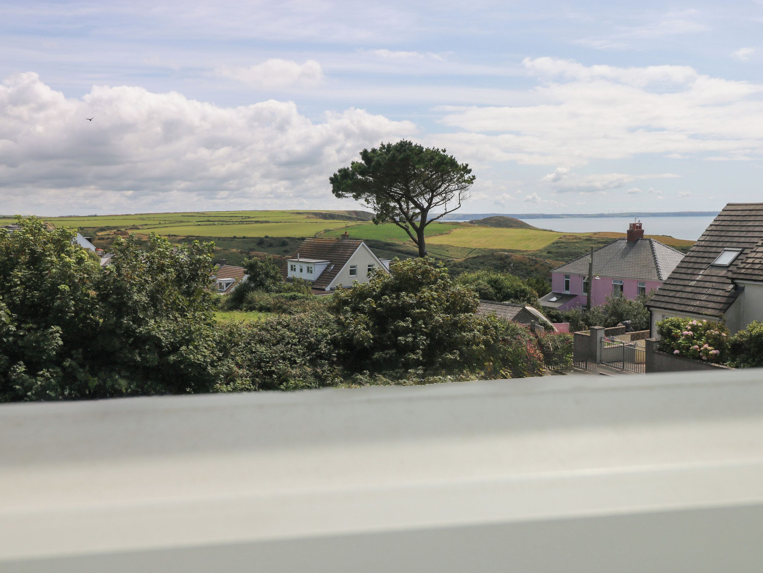 Ein Küstendorf mit Häusern, einem markanten Baum und Blick auf das Meer.
