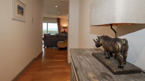 En hall med trägolv, en soffa i bakgrunden, en lampa med en lampskärm med intressant struktur och en skulptur av ett noshörning på ett bord.