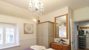 A bedroom with a bed, a dresser, a mirror, a chandelier, and a window with blinds. - The Hideout (Oakham)