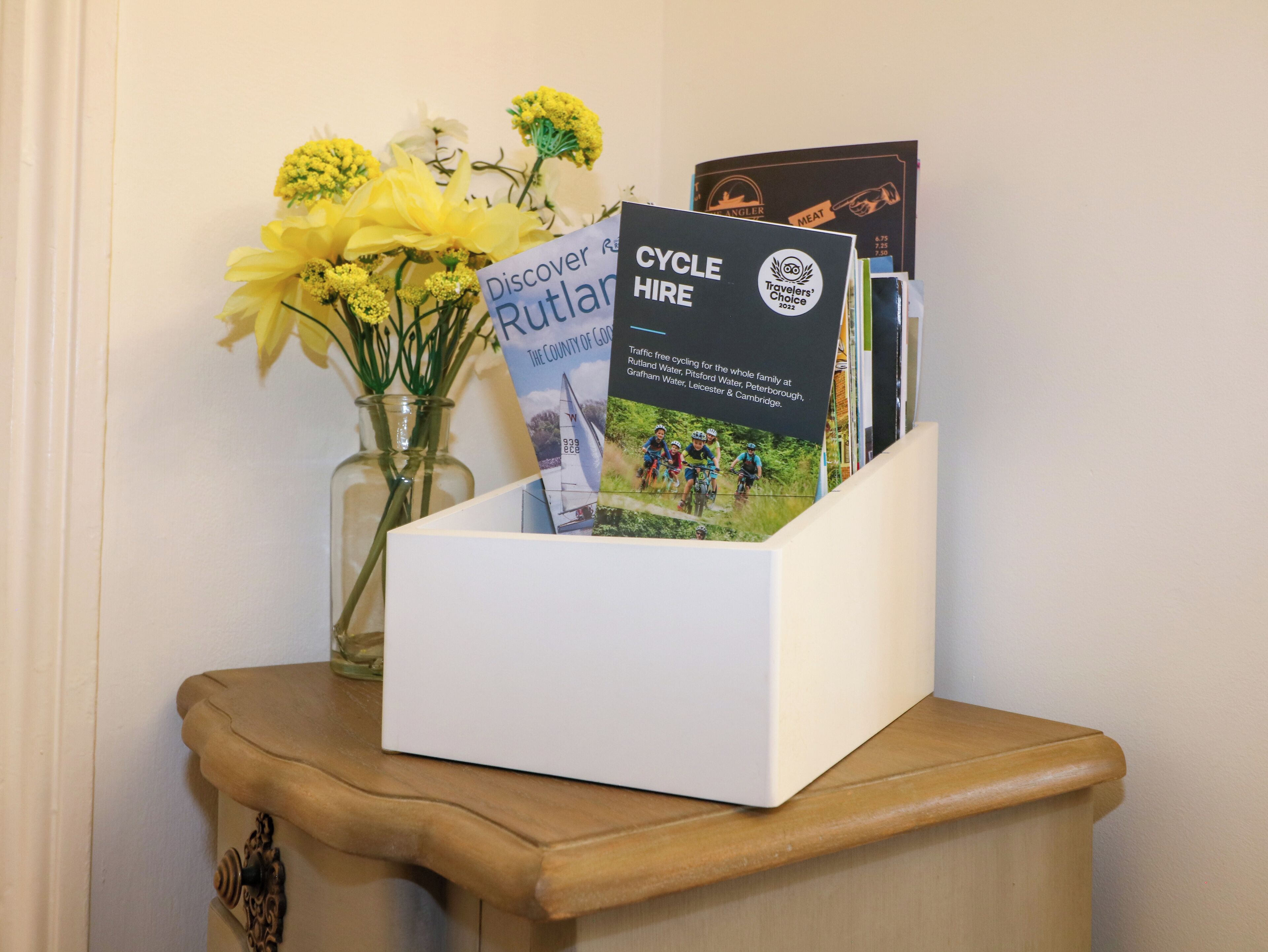 A white box with a sign for 'Discover Rutland Cycle Hire' and a vase with yellow flowers on a wooden table.