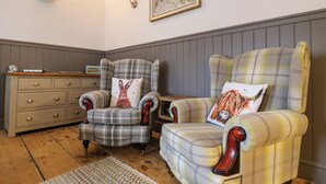 A room with two armchairs, a wooden dresser, and a framed wildlife painting on the wall. - The Hideout (Oakham)