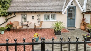 A quaint cottage with a tiled roof, a small porch with a table and chairs, and a blue door. - The Hideout (Oakham)