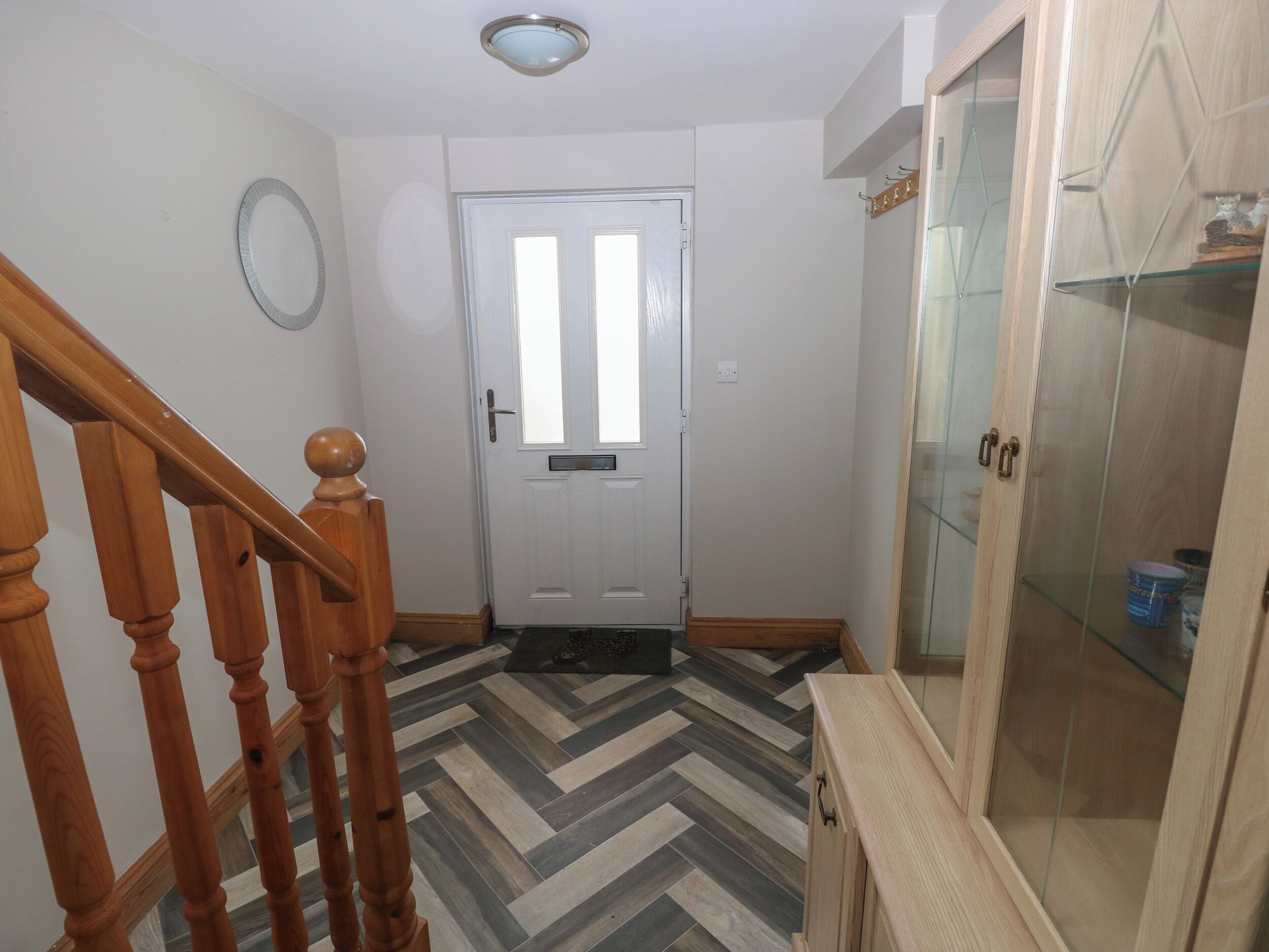 A hallway with a wooden staircase, a white door, and a glass cabinet with shelves.