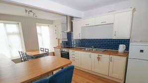 Una cocina moderna con armarios blancos, una encimera de madera y un horno empotrado. Hay dos sillas azules junto a una mesa de madera.