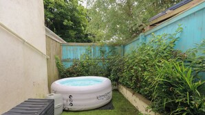 Un patio trasero con una piscina inflable desinflada, un banco de almacenamiento negro y una pequeña sección de césped artificial.