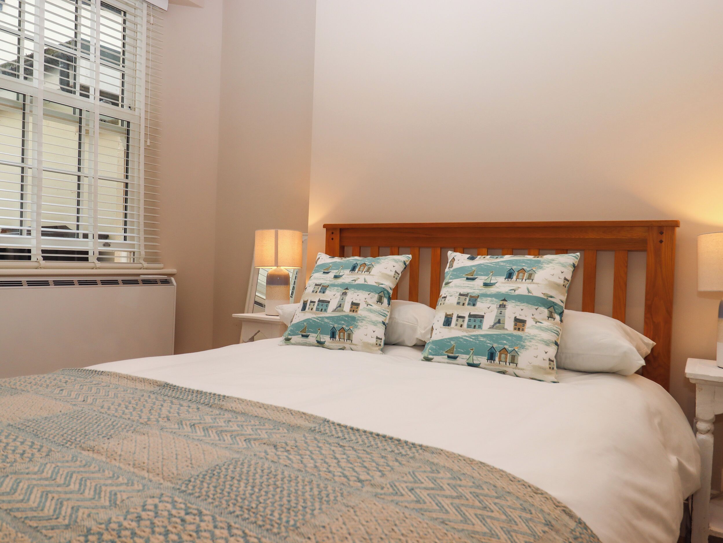 A neatly made bed with patterned pillows, a bedside lamp, and a window with blinds.