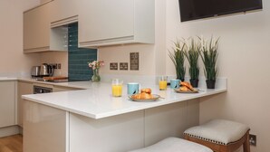 Een moderne keuken met een centraal eiland, barkrukken, een flatscreen televisie en potplanten.