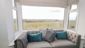 A grey sofa with teal and patterned cushions in a room with large windows overlooking a grassy field. - Glynmor (Harlech)
