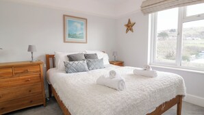 A bedroom with a wooden bed, white bedding, a star decoration, a painting, and a window with a view. - Glynmor (Harlech)