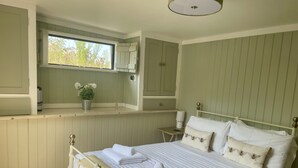 A neatly arranged bedroom with a bed, bedside tables, a window, and built-in cabinets. - The Cow Shed (Wadebridge)
