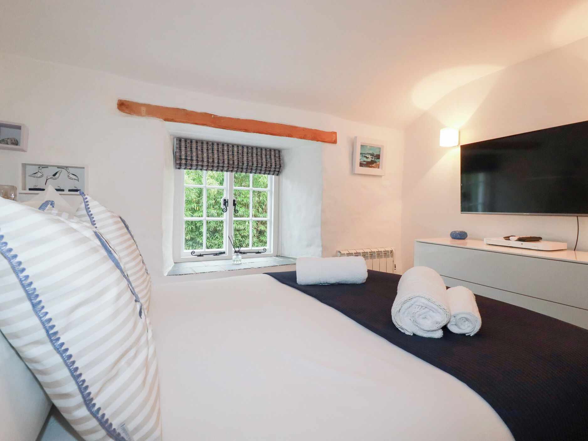 A hotel room with a large bed, a TV, a window with curtains, a bedside table, and a radiator.