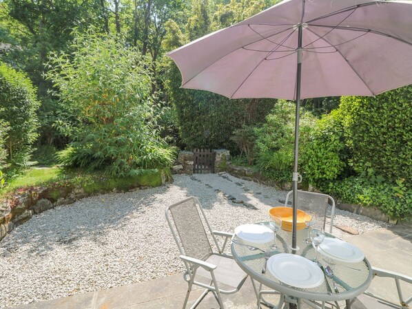 An outdoor patio with a table set for four, surrounded by lush greenery and a gravel path.