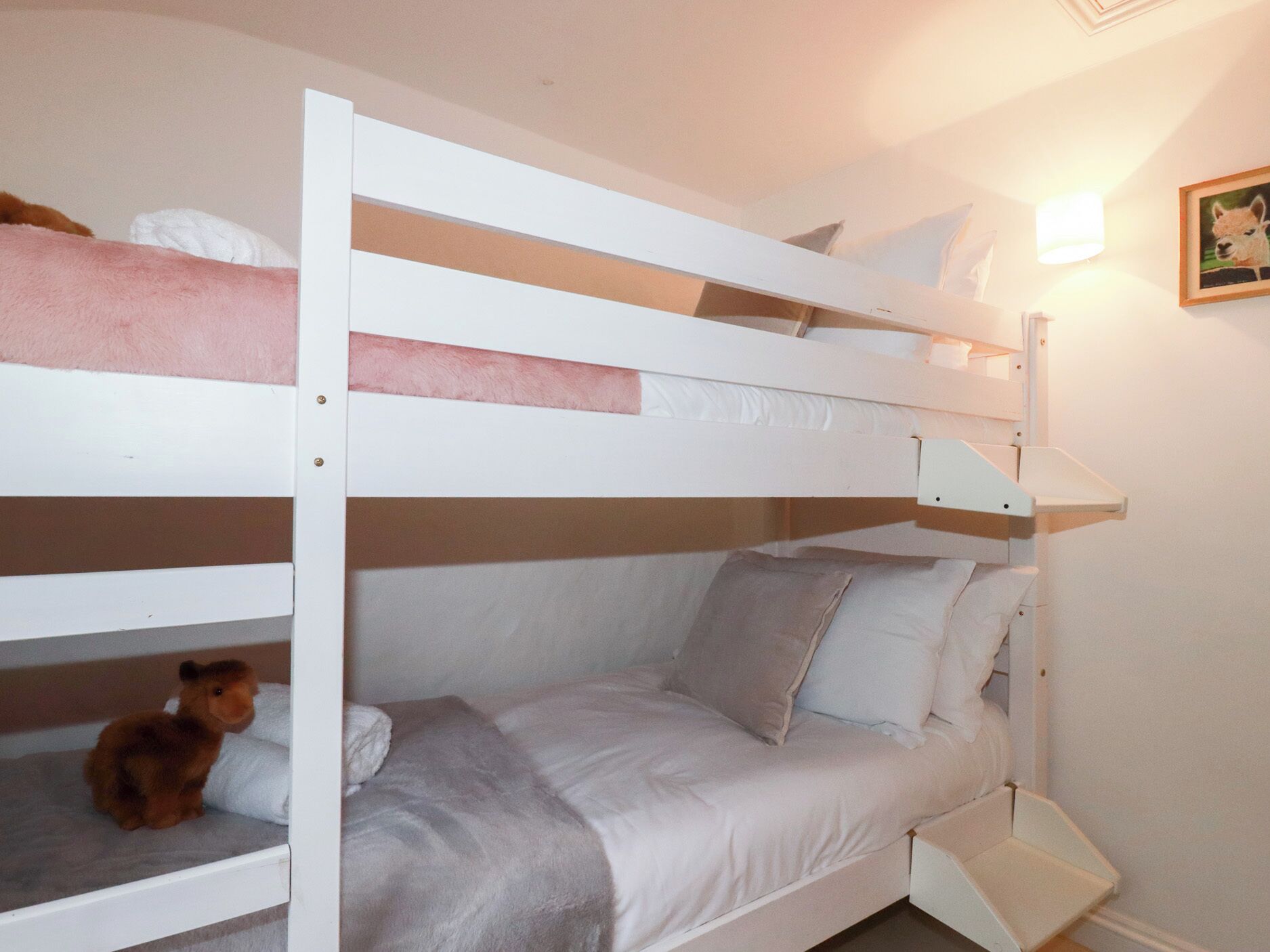A bunk bed with a teddy bear on the lower bunk and a bedside table with a lamp.