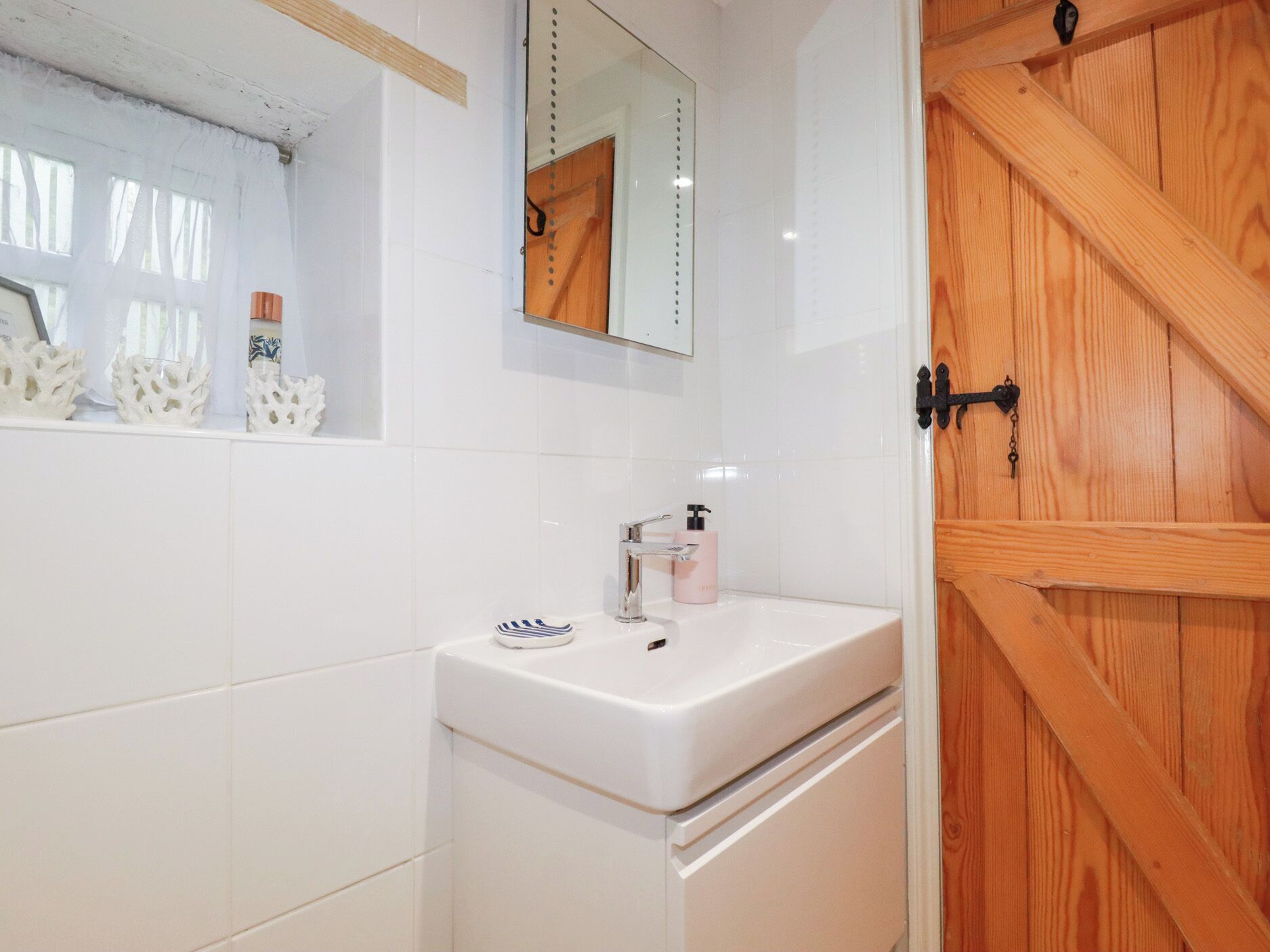 Un baño con un lavamanos blanco, un espejo y una puerta de madera.