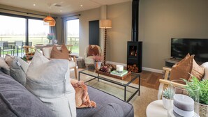 A modern living room with a sofa, coffee table, and a fireplace. - Holm Oaks Cottage (Godalming)