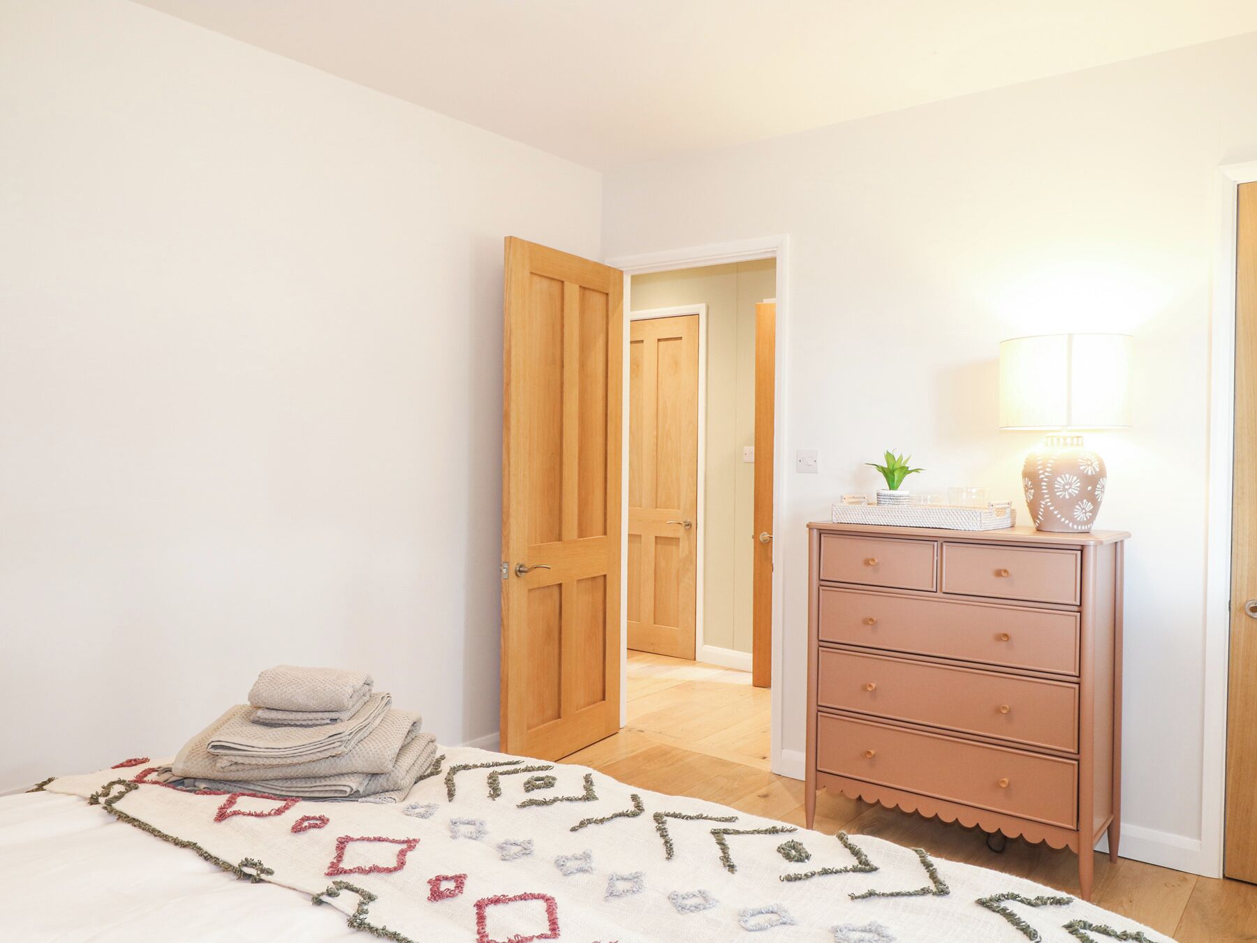 A bedroom with a bed, a dresser, a lamp, and a door leading to another room.