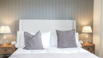 A neatly made bed with two pillows and two bedside lamps, set against a wall with vertical paneling.