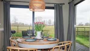 A round dining table with four wooden chairs, a woven pendant light, and a vase of red tulips. - Holm Oaks Cottage (Godalming)