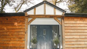 A wooden building with a dark door, two potted plants on either side, and a small porch area. - Holm Oaks Cottage (Godalming)