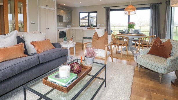 A modern living room with a sofa, coffee table, and dining area. - Holm Oaks Cottage (Godalming)