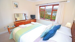 A bedroom with a bed, a dresser, a television, a window with a view of the countryside, and a painting on the wall. - Artist's Cottage (Penrhyndeudraeth)