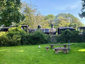 Een tuin met een stoomtrein, picknicktafels en een witte zwaan.