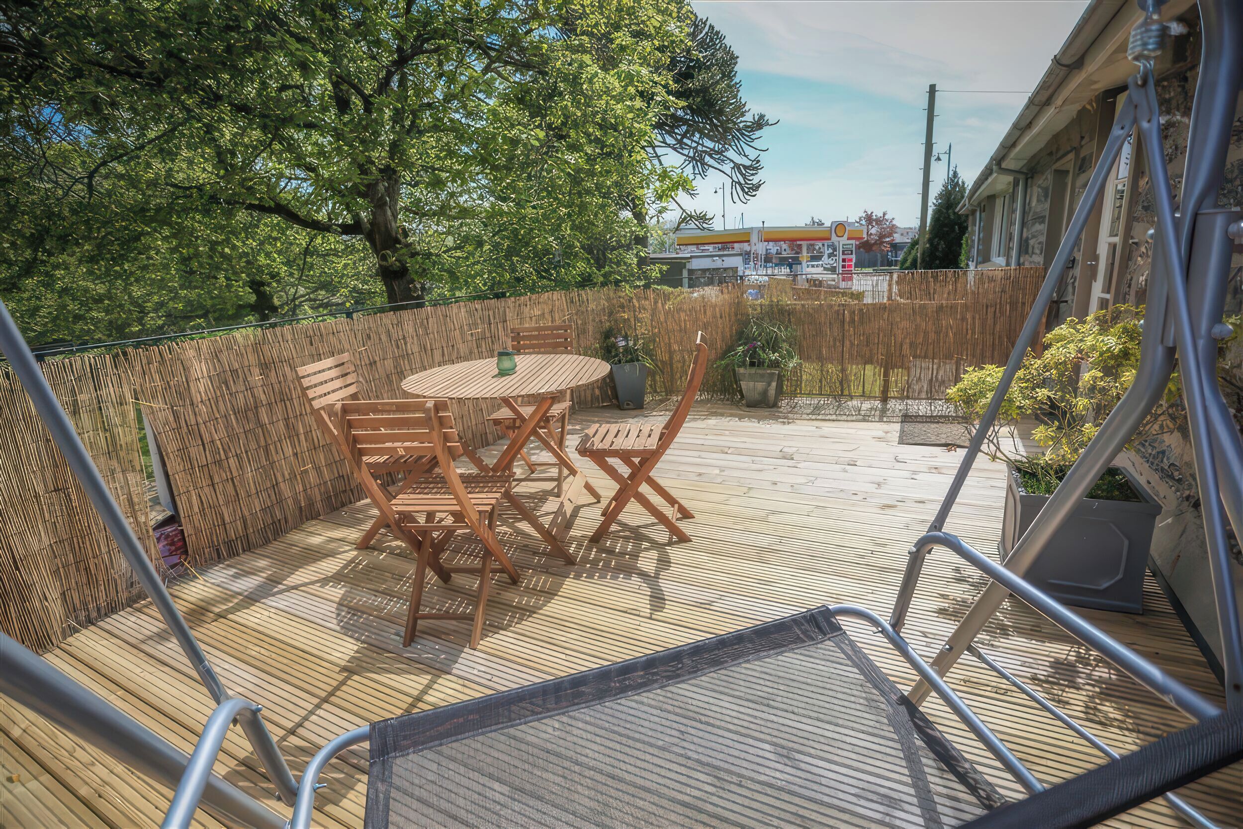 An outdoor patio with a wooden table and chairs, surrounded by a bamboo fence and potted plants.