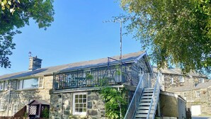 A stone building with a balcony, a staircase, and a fenced garden area. - Treetops Flat (Porthmadog)
