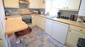 A compact kitchen with white cabinets, a wooden countertop, a dishwasher, a toaster, and a coffee maker. - Treetops Flat (Porthmadog)