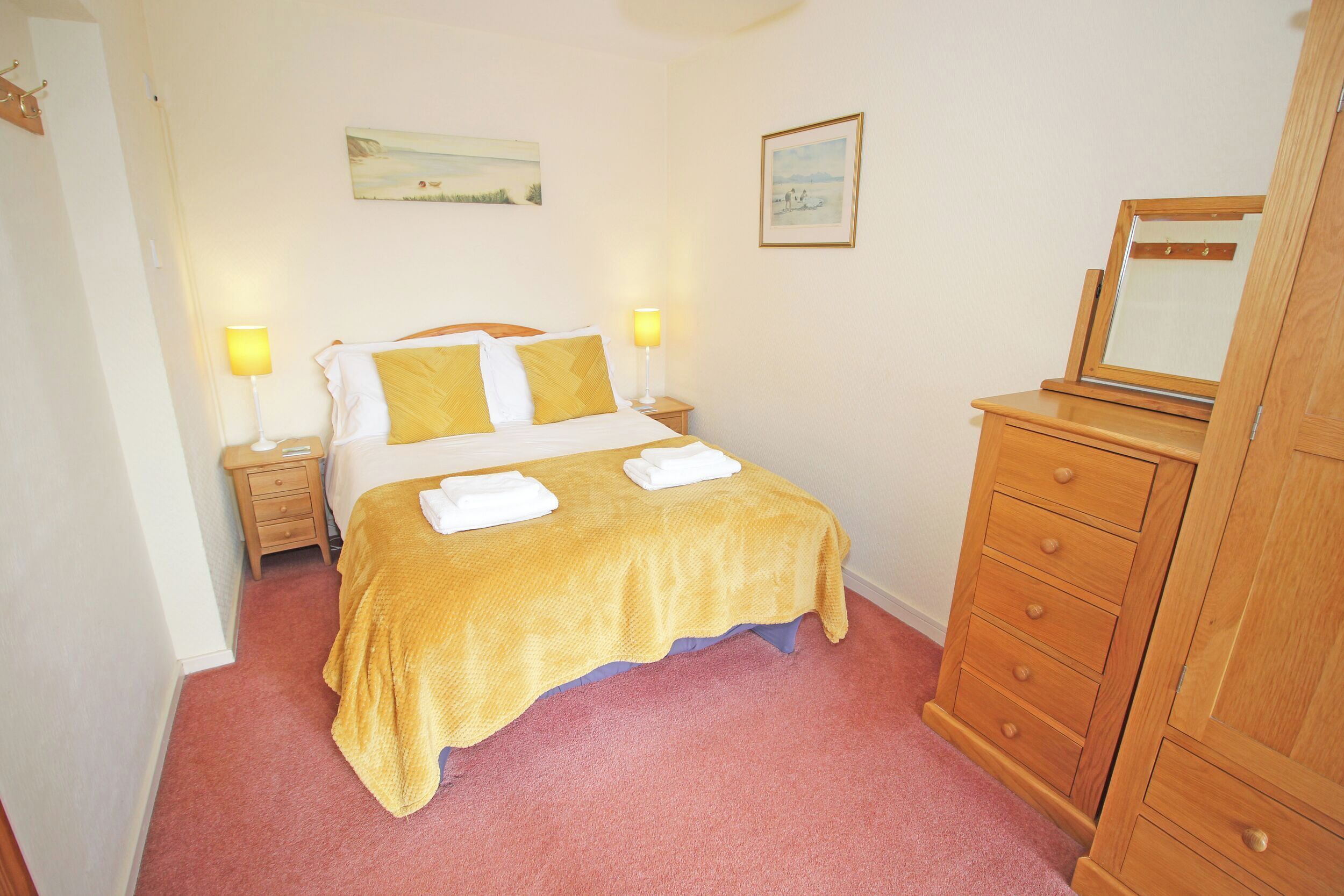 A bedroom with a bed, two bedside lamps, a wooden dresser, and a mirror.