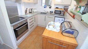 A compact kitchen with a stove, oven, microwave, and a small sink. - Glaslyn Harbour Views (Porthmadog)