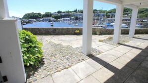 A covered outdoor area with stone flooring and white pillars, overlooking a harbor with boats and buildings. - Glaslyn Harbour Views (Porthmadog)