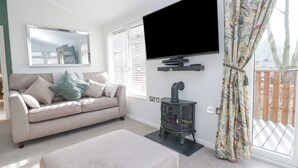 A living room with a sofa, a flat-screen TV mounted on the wall, a fireplace, and a window with curtains. - Swifts Reach Lodge (Windermere)