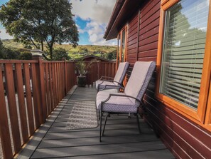 A wooden deck with two chairs and a rug, overlooking a scenic landscape. - Swifts Reach Lodge (Windermere)