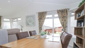 A dining area with a wooden table, brown leather chairs, a bookshelf, and a view of the backyard through large windows. - Swifts Reach Lodge (Windermere)