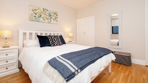 Une chambre à coucher comprenant un lit, des tables de chevet, une commode, une armoire, un miroir et un tableau accroché au mur.