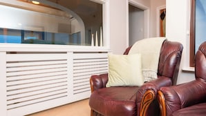 Un fauteuil en cuir avec un coussin, un radiateur blanc et une fenêtre donnant sur l’extérieur.