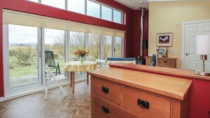 A modern kitchen with large windows, a wooden dining table with chairs, and a herringbone wood floor. - Tirlaggan Studio (Oban)